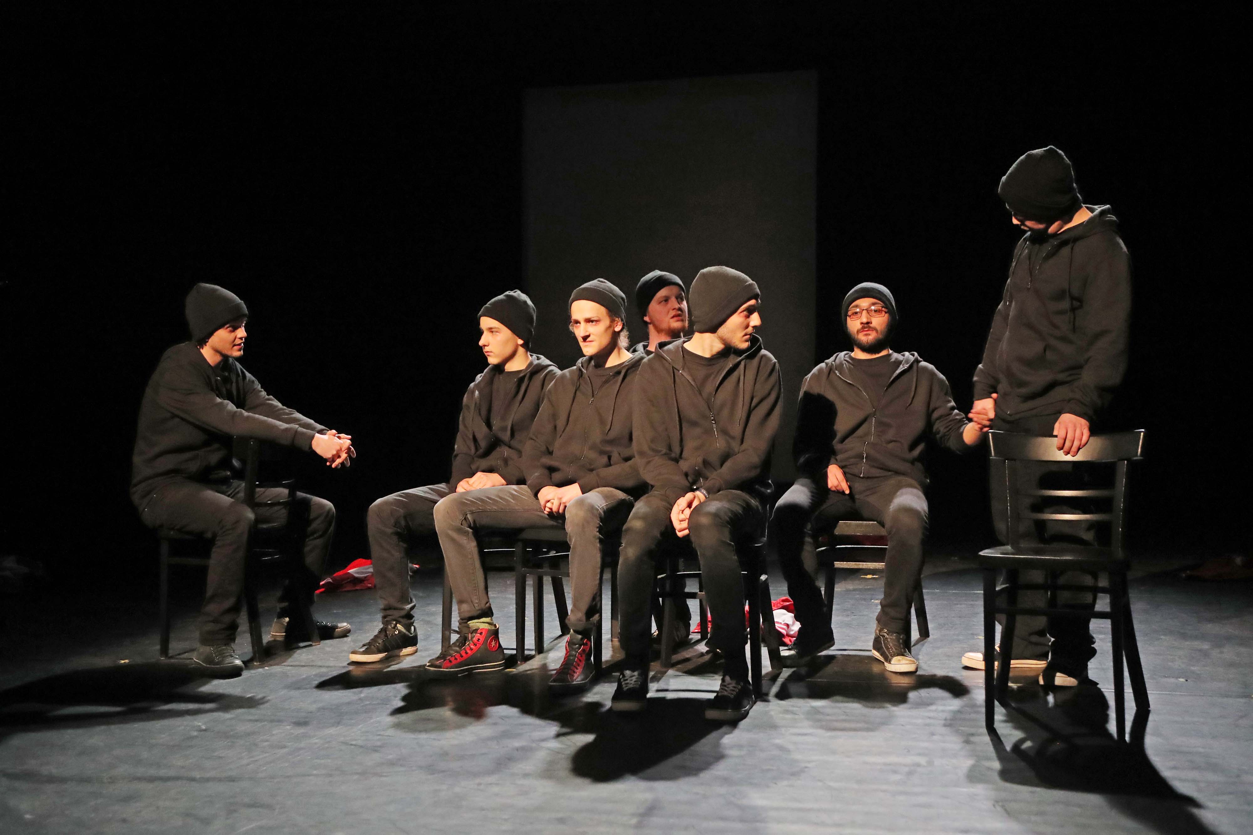 Jona wird von sieben Schauspielern dargestellt, alle sind dunkel gekleidet und haben eine schwarze Mütze an